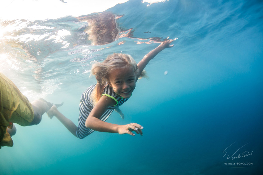 A little girl underwater with sunshine smile. Cute child does not afraid to open eyes in salt water